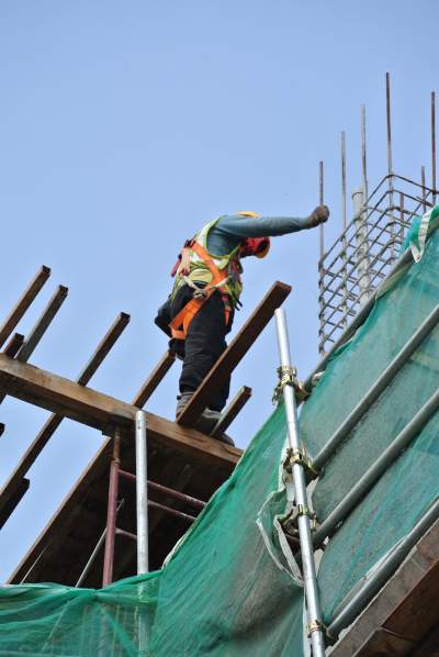 Ouvrier du bâtiment se dresse sur des planches branlantes sur un chantier de construction en altitude et baisse les yeux