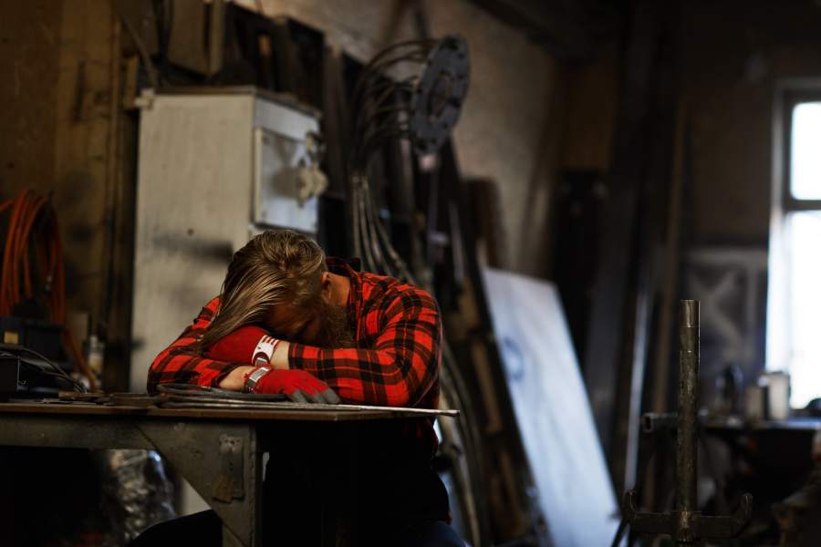 le travailleur fatigué qui dort la tête sur les bras à une table en milieu de travail a besoin de repos pour réduire la fatigue